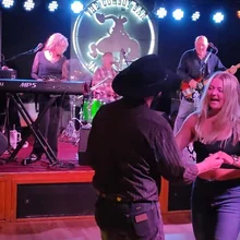 Couple dancing in front of a live band performing on stage with colorful lights at a bar